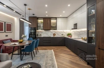 Открытое пространство кухня-гостиная в современном стиле: тёплый ореховый пол, угловая кухня с тёмно‑графитовыми нижними и белыми верхними фасадами, высокими шкафами под орех и стеклянными витринами, мраморным фартуков и подсветкой рабочей зоны. В гостиной зоне бордовый диван, светло‑серая мягкая мебель, овальный деревянный стол с синими стульями, голубой ковёр, бордово‑синие текстильные акценты, настенные постеры и живые растения, создающие уютную атмосферу.